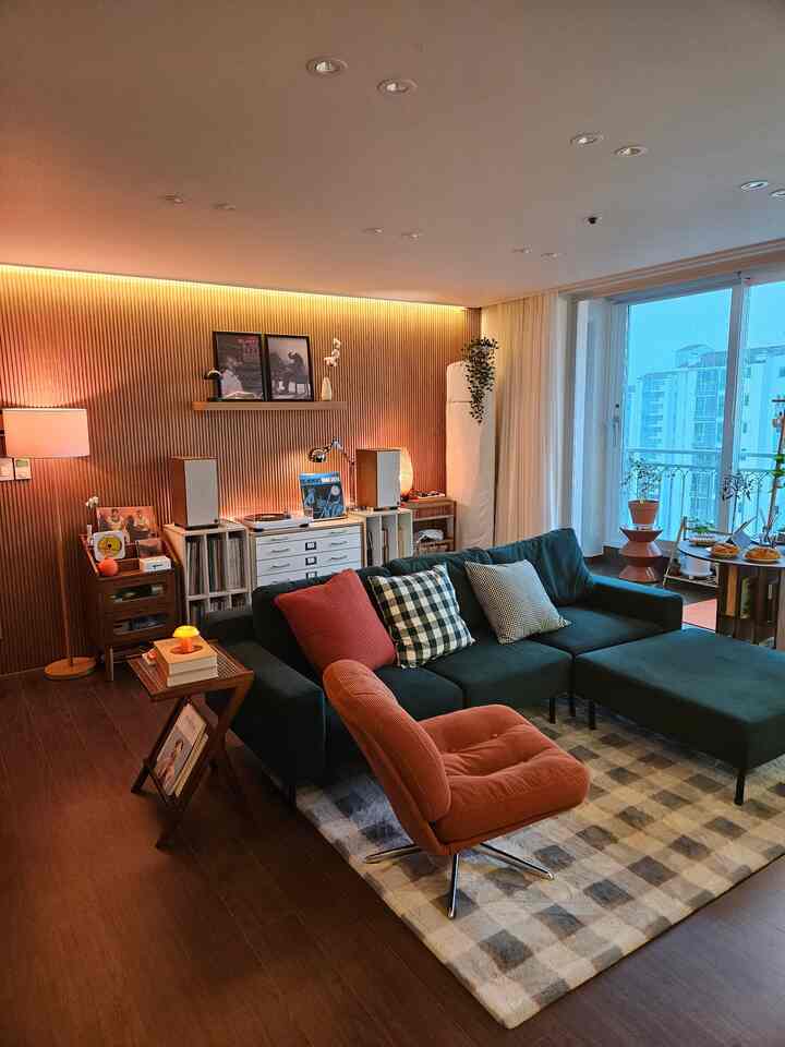 温かみのある木目調の壁とダークグリーンのソファが配置されたリビング、オレンジ色のアームチェアと居心地の良いラグがあるインスタ映えの空間