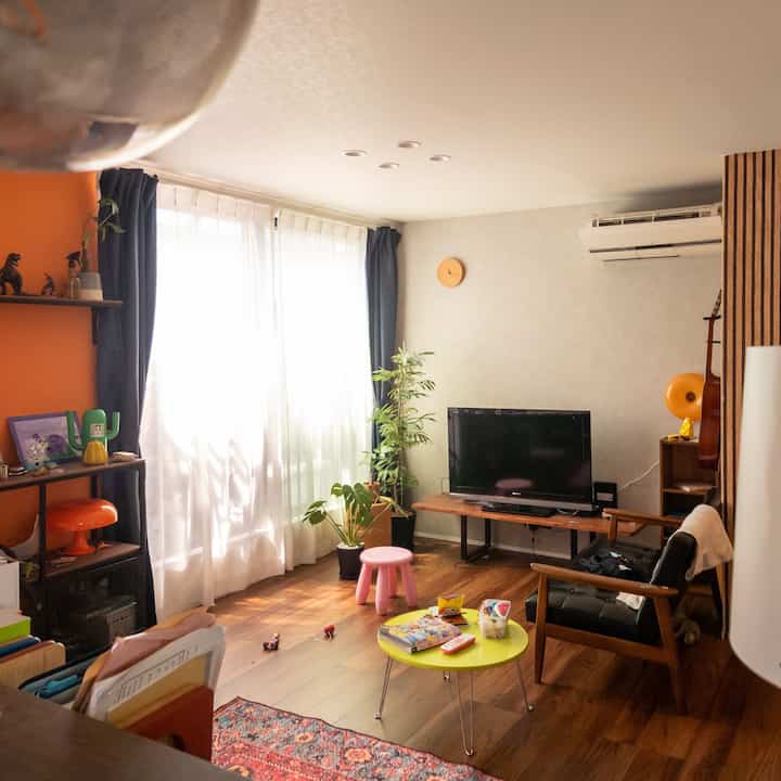 Natural modern living room with wood tones and blue curtains, featuring TV, plants, and a pink stool
