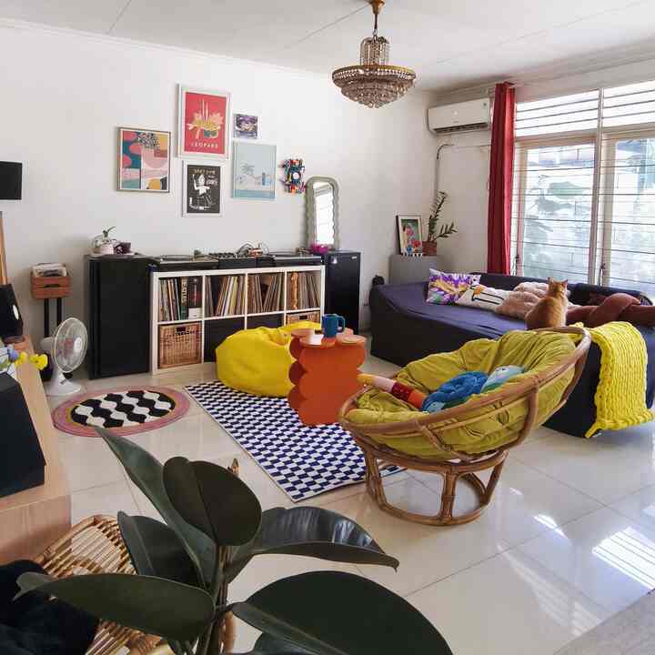 Bright natural-toned living room featuring a large sofa, yellow bean bag, checkered rug, and a cat creating a cozy atmosphere