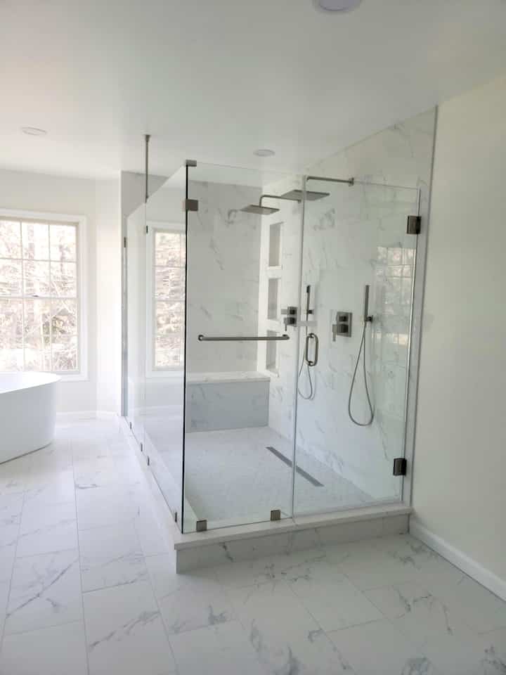 Bright white-toned bathroom featuring a glass enclosed two-person shower booth and freestanding tub on the left, with modern design