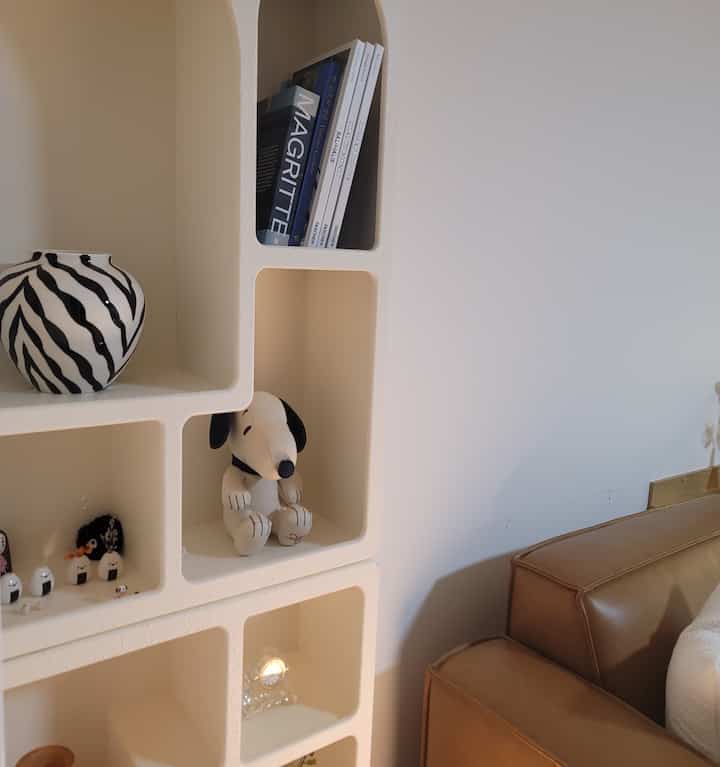 Natural color living room featuring a brown leather sofa and white geometric arched wall shelf with decorative items
