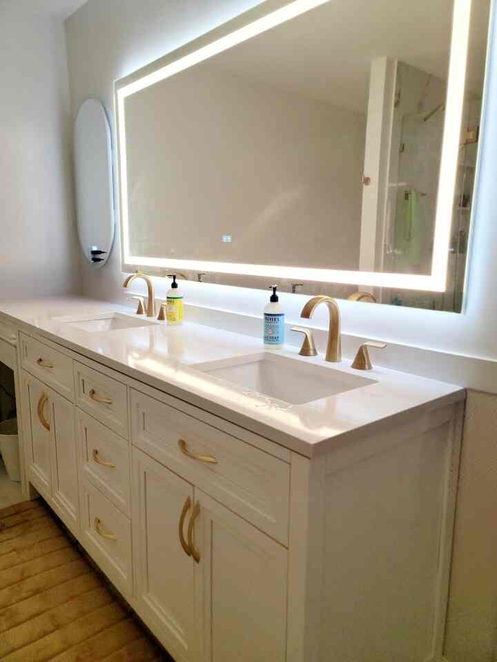 White and gold toned bathroom featuring a large LED-lit mirror and clean vanity with elegant gold handles