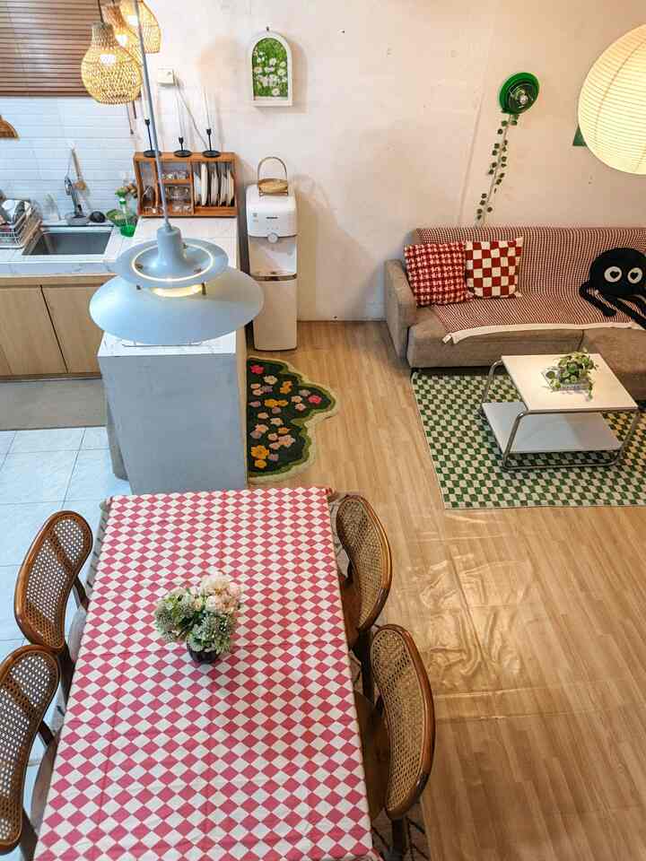 Natural brown and red toned studio apartment living room and kitchen featuring checkered tablecloth and rattan chairs in a cozy setting