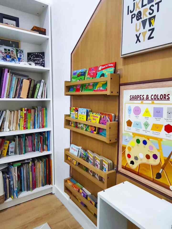 White walls and wood-tone bookshelves featuring children's books and posters in a kids' room