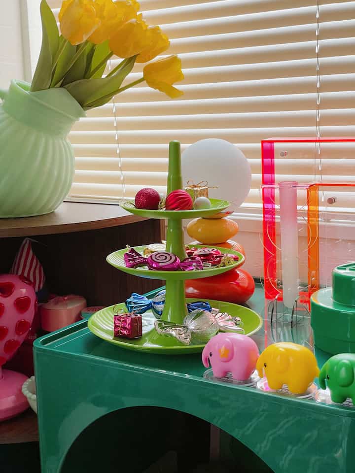 明るい黄色のチューリップが飾られた淡い緑の花瓶と、カラフルなオブジェが乗った緑の三段トレーが配置されたレトロな雰囲気のインテリア