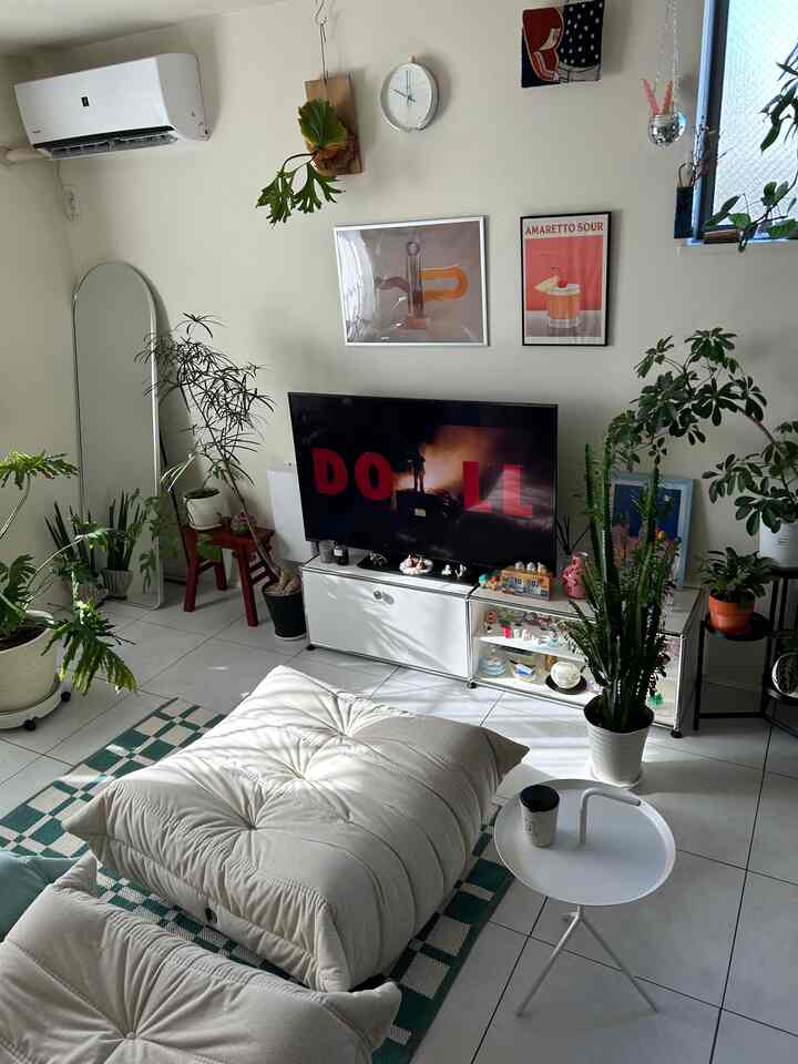 白とナチュラルな色調のリビング、テレビ台とふかふかの床クッション、多様な植物が調和した雰囲気のあるインテリア