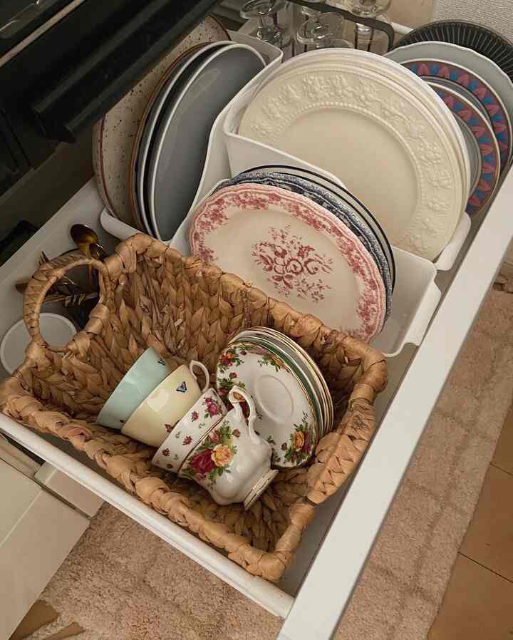 白とベージュのトーンのキッチンの引き出しにきれいに収納された皿とティーカップが見える収納スペース