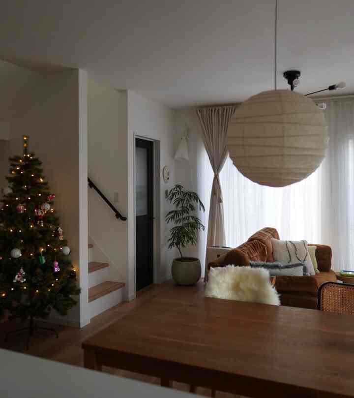 白い壁とブラウンのソファが配置されたナチュラルなトーンのリビング、左側にストリングライトが飾られたクリスマスツリーがある印象的な空間