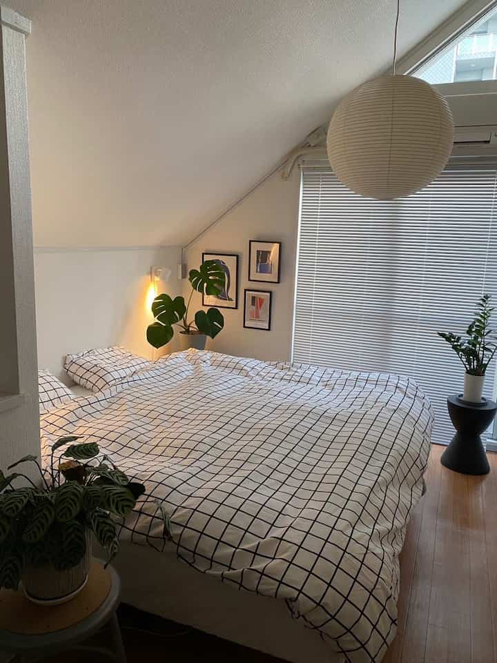白と黒のチェック柄掛け布団カバーがあるミッドセンチュリーモダン風の落ち着いた寝室、観葉植物と間接照明が配置された雰囲気のあるインテリア