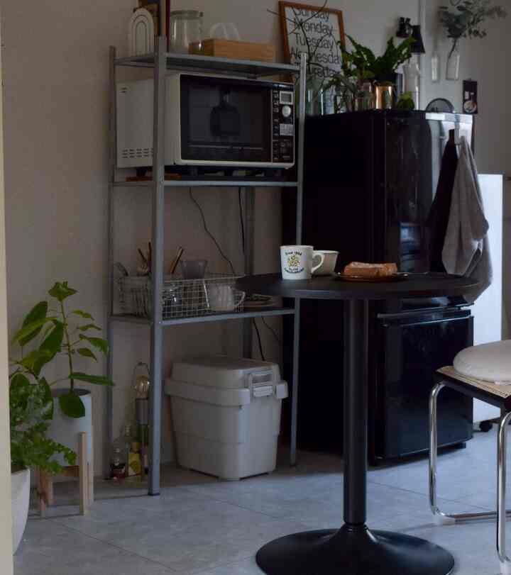 黒とグレーのトーンのダイニングルーム、丸いカフェテーブル、冷蔵庫、棚、観葉植物が配置された雰囲気のあるインテリア