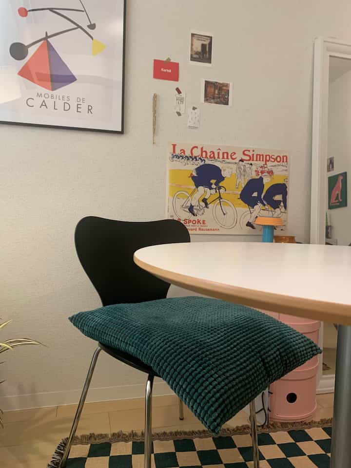 A dining room with white table and black chair, pink storage unit and colorful posters creating a modern setting
