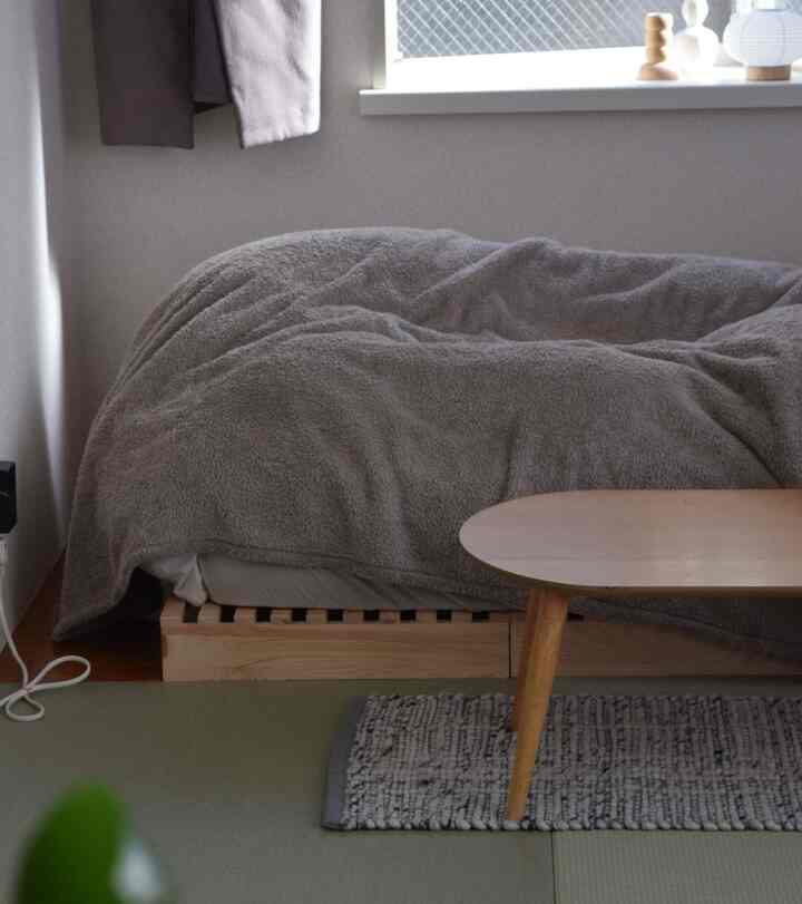 ベージュ色調のワンルーム寝室、ナチュラルな木製家具と暖かい毛布が配置された落ち着いた空間