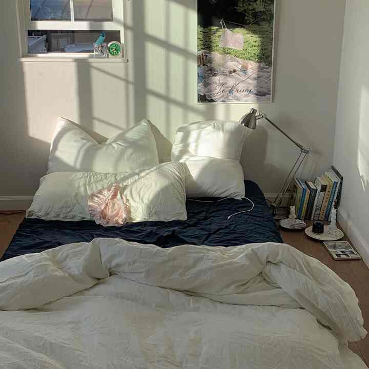 Sunlit white-toned simple bedroom featuring a bed, reading lamp, and poster with a cozy atmosphere