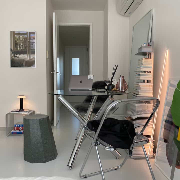 Modern home office space in white and silver tones featuring glass desk and metal chair in a clean interior