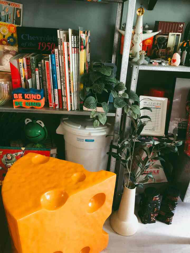明るい黄色のチーズ型ミニテーブルと金属製の棚、多様な小物と植物が配置された個性的なリビングスペース