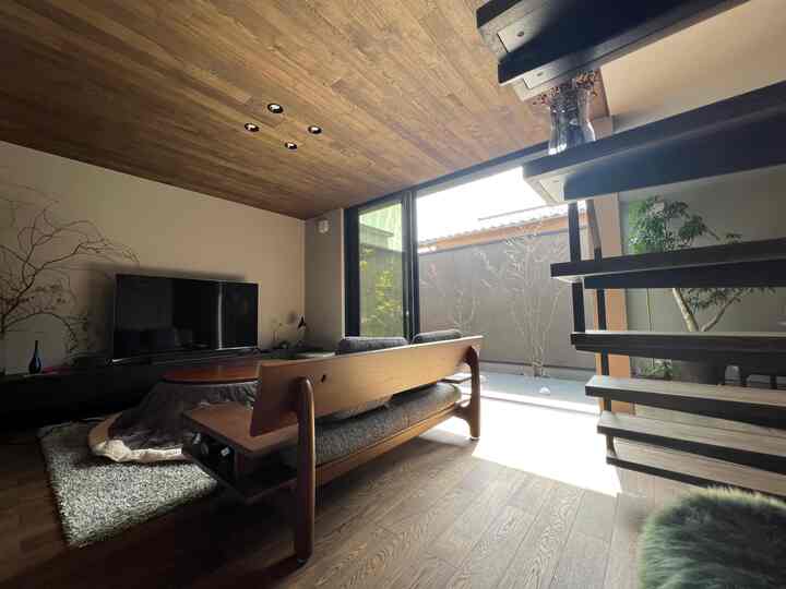 Warm brown wood tones and large windows define a modern living room, featuring a sofa and TV stand with natural ambiance