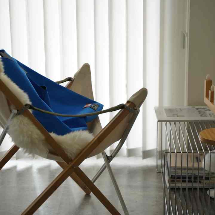 明るいホワイトトーンとウッドトーンのミニマルモダンなリビング、青いアウトドアチェアと白いカーテンが配置された空間