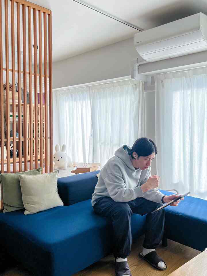 落ち着いたブルーとアイボリーの色調のリビング、広いコーナーソファと木製スラット仕切りが配置された快適な在宅勤務空間