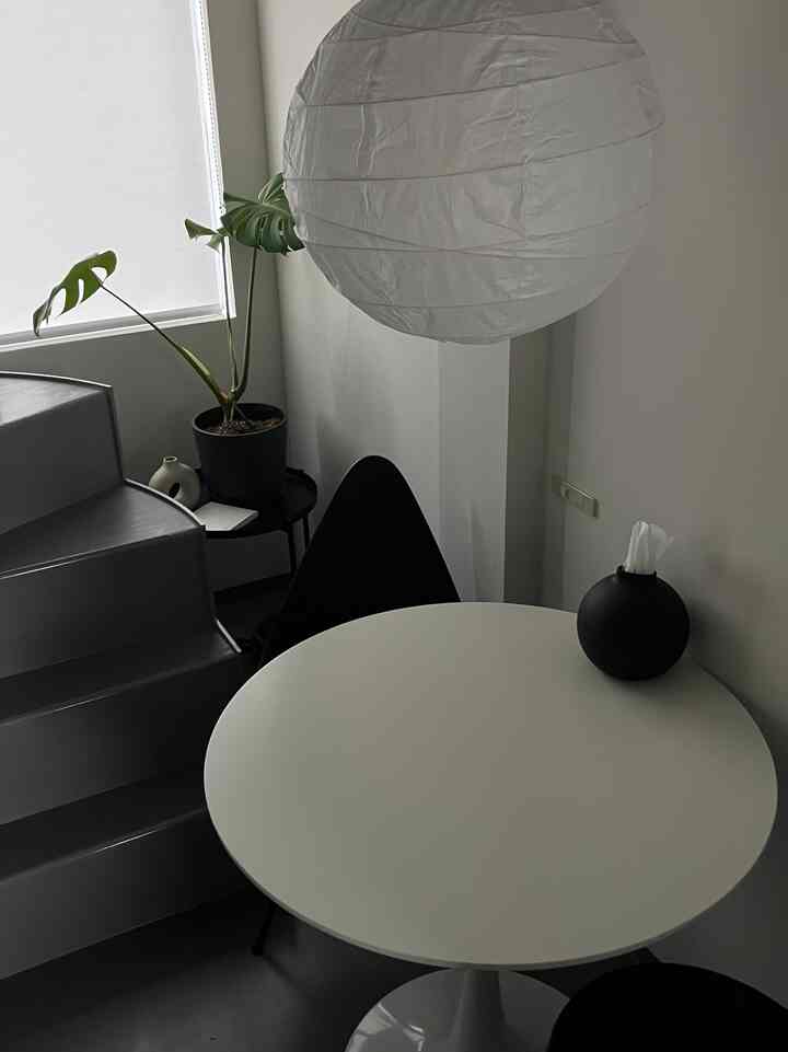 白と黒のトーンでまとめられたミニマルなワンルームのダイニングスペース、金属製の階段と植物が配置された清潔感のあるインテリア