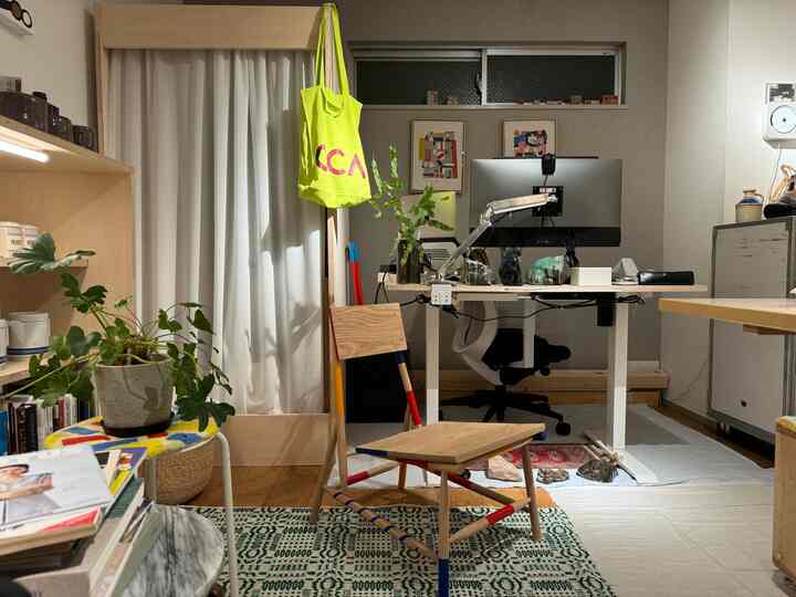 明るい木目調と白を基調としたワンルームのホームオフィス空間、木製の机と椅子、植物、壁の絵が配置されたシンプルモダンなインテリア