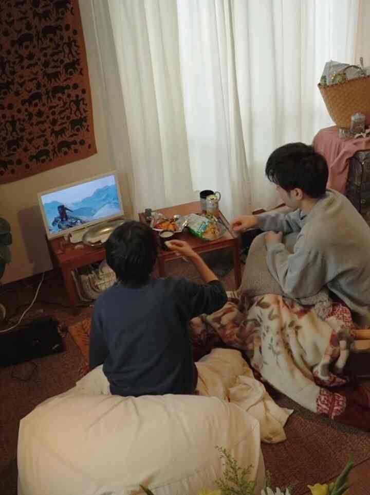 ナチュラルな色調の狭い寝室、ビーズクッションとラグ、スナックが置かれた小さなテーブルが配置された雰囲気のあるホームシネマ空間