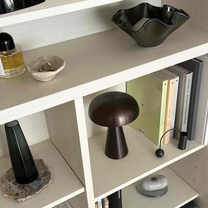 ナチュラルカラーの本棚空間、テーブルランプとボウルが整然と配置されたミニマルなインテリア