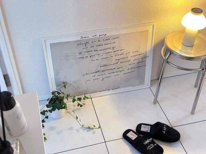 白いタイル床とステンレスのスツール、テーブルランプが配置されたミニマルな玄関の印象的な空間