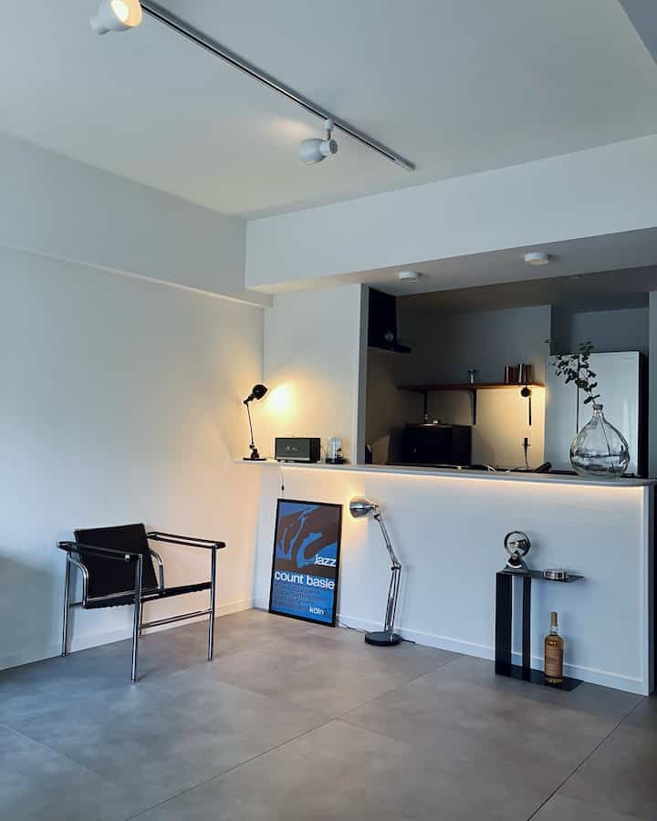 White and gray toned kitchen and adjacent living space featuring mid-century modern side table and lamps in a simple interior