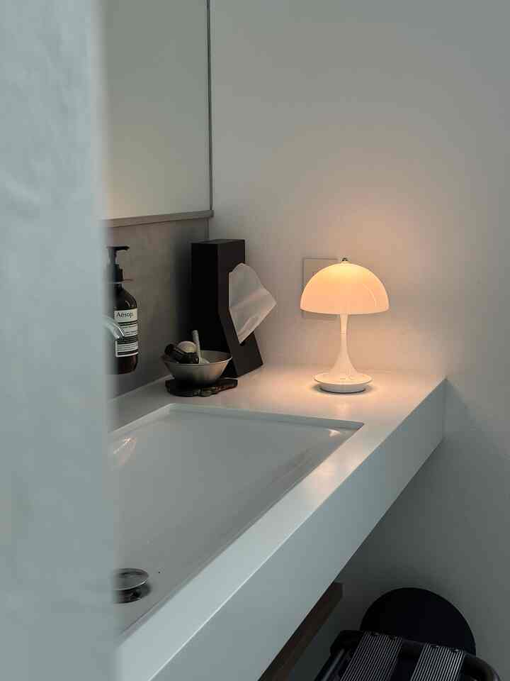 シンプルモダンな白を基調とした洗面台空間、パントレラテーブルランプが暖かい雰囲気を演出する印象的なインテリア