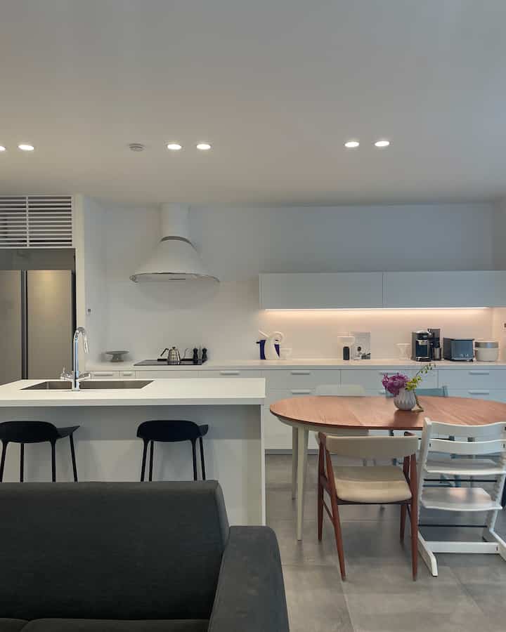 Modern kitchen and dining room with white and natural tones, featuring a wood dining table and diverse chairs in a neat setting