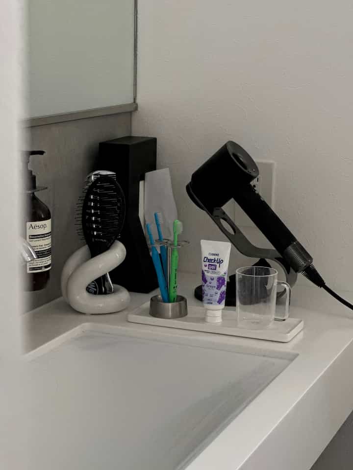 白を基調としたバスルームの洗面台、セラミックの歯ブラシ立てとダイソンのヘアドライヤーが配置されたミニマルな空間