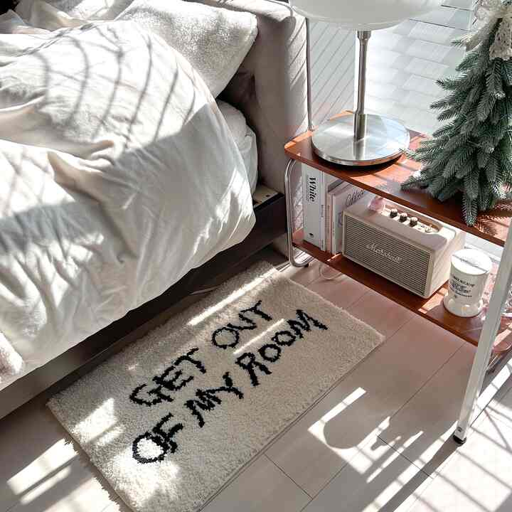 明るい白色の6畳寝室、ベッドの横に白い文字入りラグとナイトテーブル、フロアランプが配置された雰囲気のあるインテリア