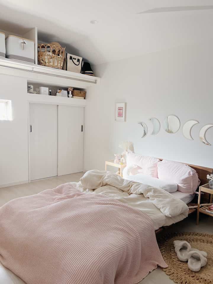 Soft pink and beige bedroom featuring a wooden bed and crescent moon mirrors, creating a cozy atmosphere