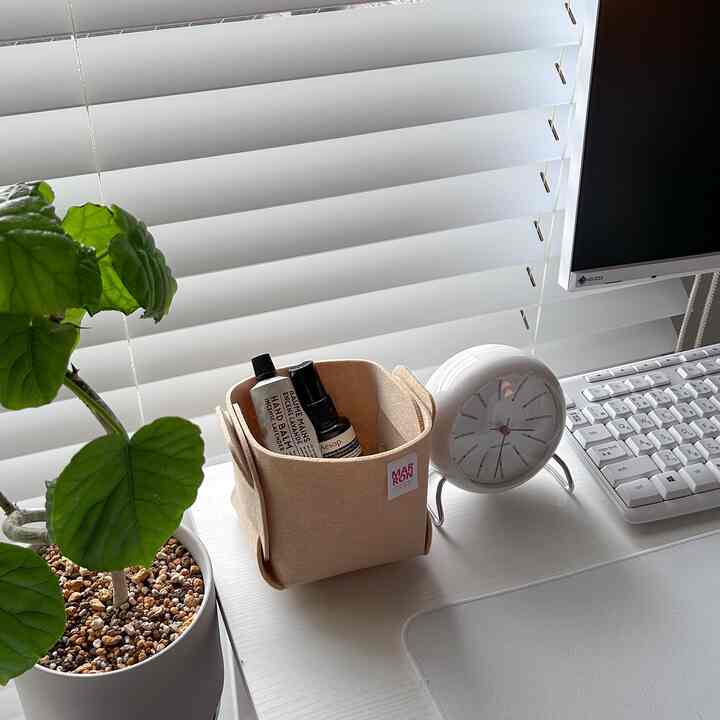 白とベージュのトーンのホームオフィスデスク、植物とアルネ・ヤコブセンの時計が配置された清潔感のある空間