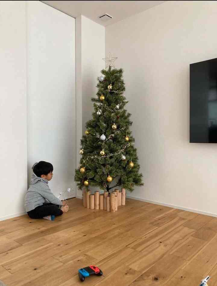 ナチュラルな色調のリビング、クリスマスツリーとゴールドのオーナメントが飾られ、子供が床に座っている印象的な空間