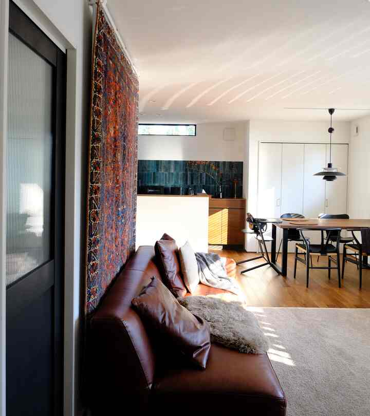 明るい白い壁と木目調の床、ブラウンのレザーソファとダイニングが配置された温かみのある自然なリビング空間