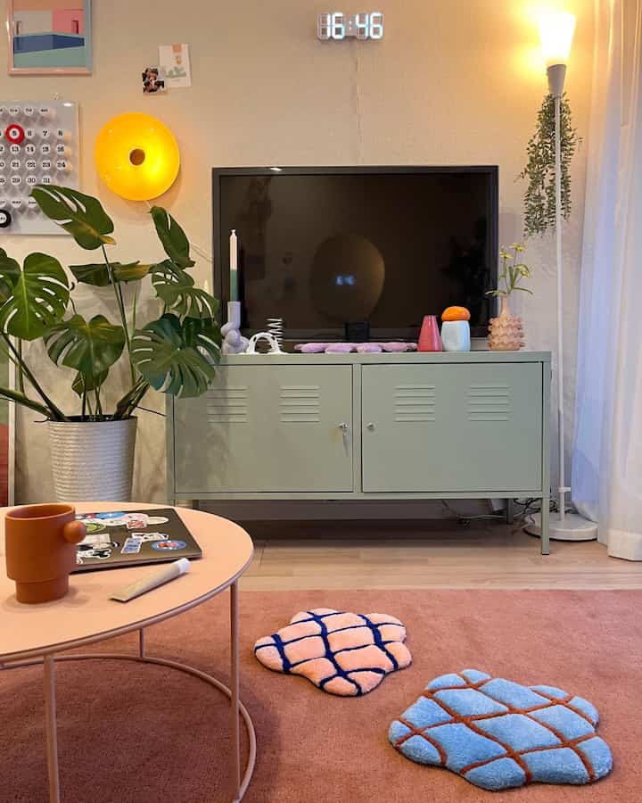 ナチュラルカラーのリビング、ピンクのラグ、ミント色の鉄製キャビネットと緑の植物が配置された雰囲気のある空間