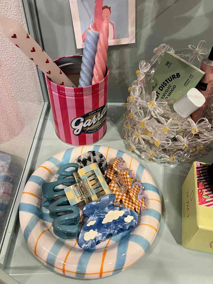 ピンクとブルーのストライプ模様のトレイに複数のヘアクリップとピンクのキャンドルが置かれたかわいらしいディスプレイスペース