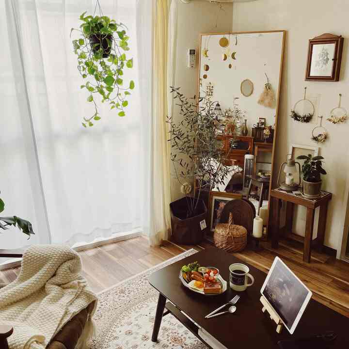 Brown natural-toned living room featuring a central dining table with breakfast, surrounded by plants and a large mirror, creating a cozy cafe-style space
