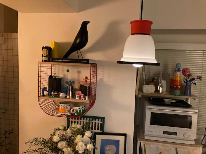 Kitchen space with white walls and natural wood shelves, highlighted by a black bird decoration and a red pendant light, creating a cozy atmosphere