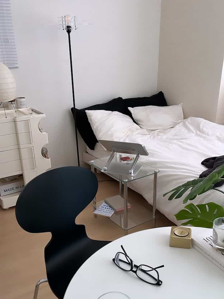 ナチュラルな色調の寝室、白い壁と木目の床、黒いチェアとフロアランプが配置されたミニマルな一人暮らしの空間