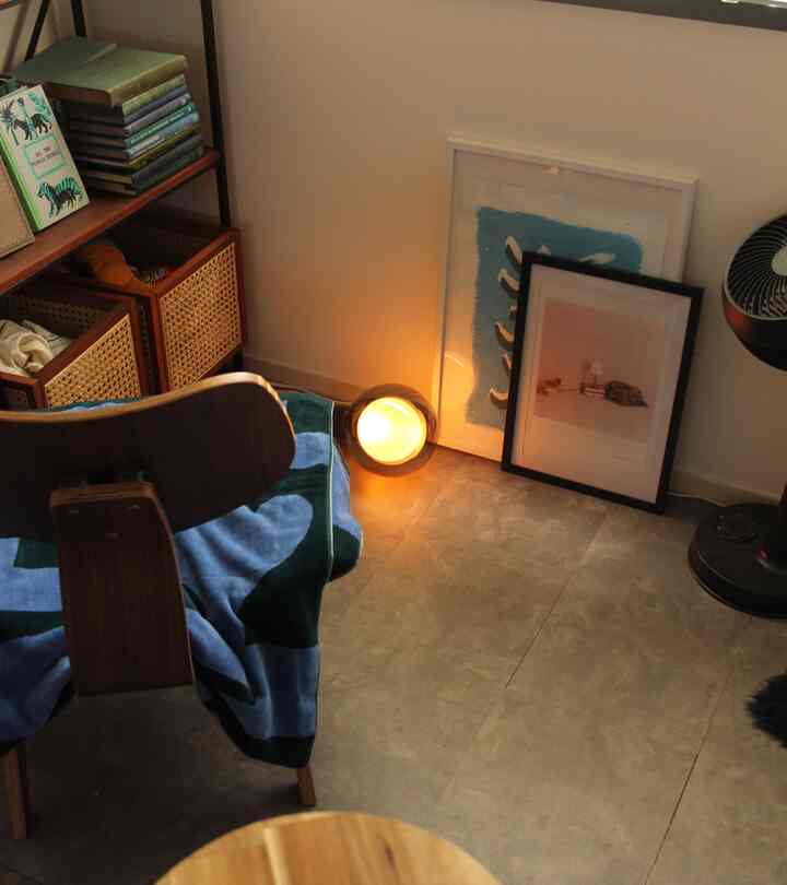 白い壁とナチュラルな木製家具が調和した狭い部屋、床に置かれたフロアランプとウォールアートが雰囲気のあるインテリアを演出