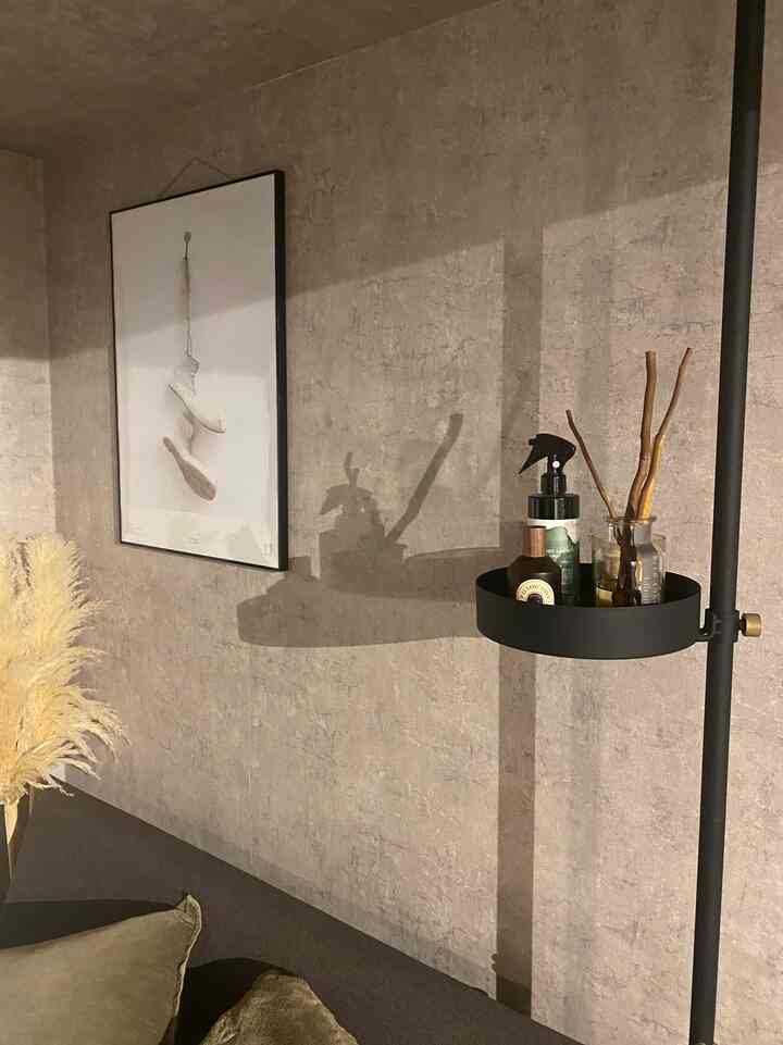 Natural-toned bedroom with concrete wallpaper, featuring a poster and diffuser on a drawer line shelf, creating a modern and vintage atmosphere