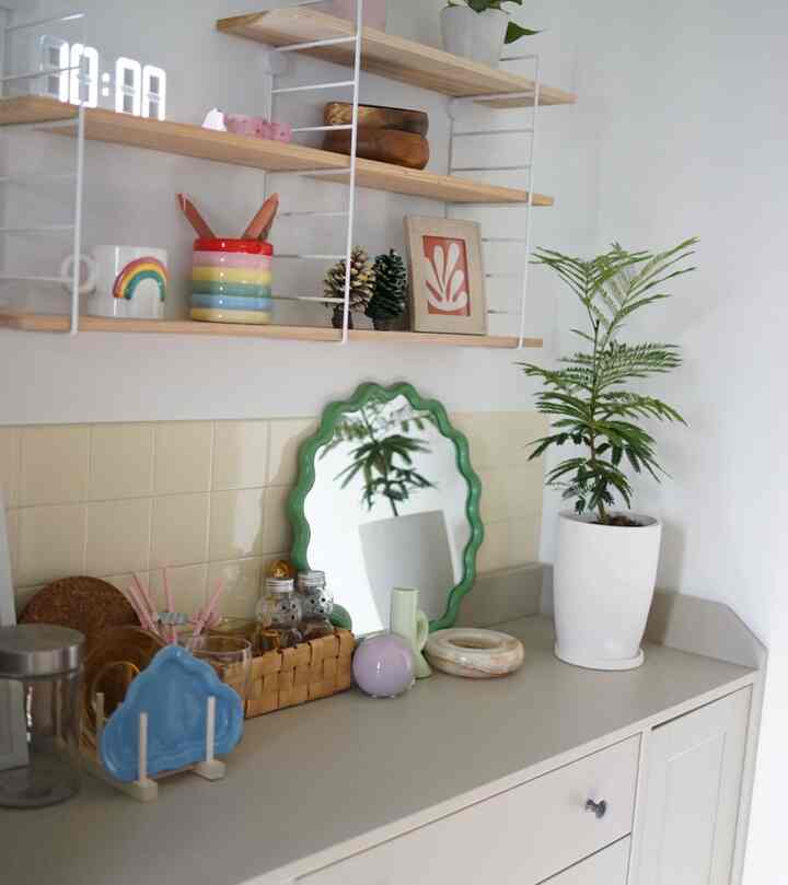 白とベージュの壁とキャビネットが背景のキッチン空間、ナチュラルな木製棚と多彩な小物、緑の植物が配置された雰囲気のあるインテリア