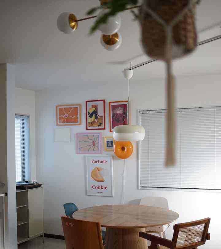 白い壁と木目調の丸いダイニングテーブル、カラフルなポスターとラタンチェアが配置された印象的なダイニングルーム