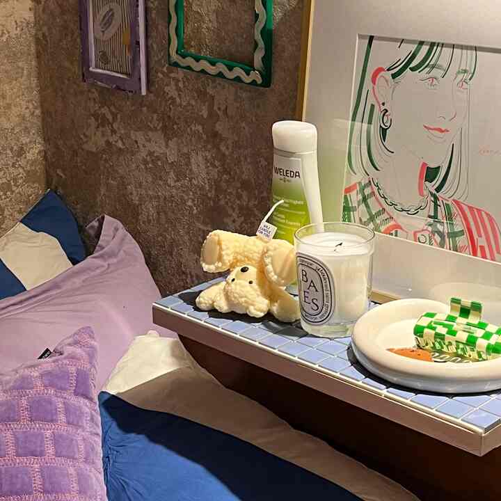 パープルとナチュラルカラーの寝室、パープルの枕、かわいいオブジェ、キャンドル、額縁が配置された温かみのある空間