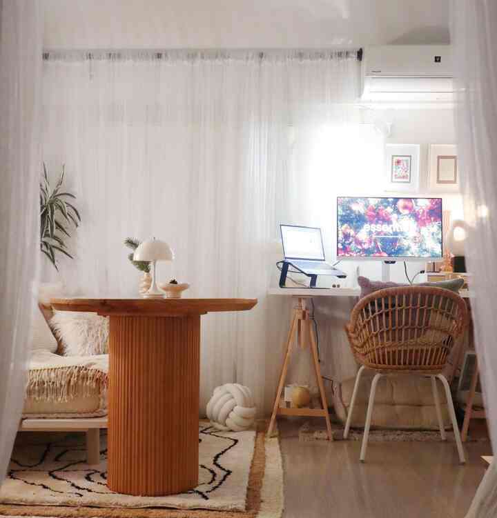 Natural-toned living room and home office space featuring a rattan chair and round wooden dining table with cozy ambiance
