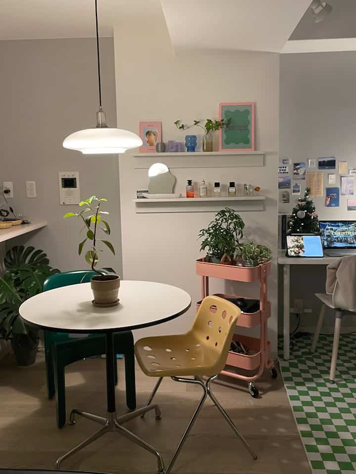 ホワイトとグリーンのトーンのダイニングルーム、円形テーブルとカラフルな椅子、ピンクのキッチンワゴンがリラックスしたおうちカフェの雰囲気を演出する空間