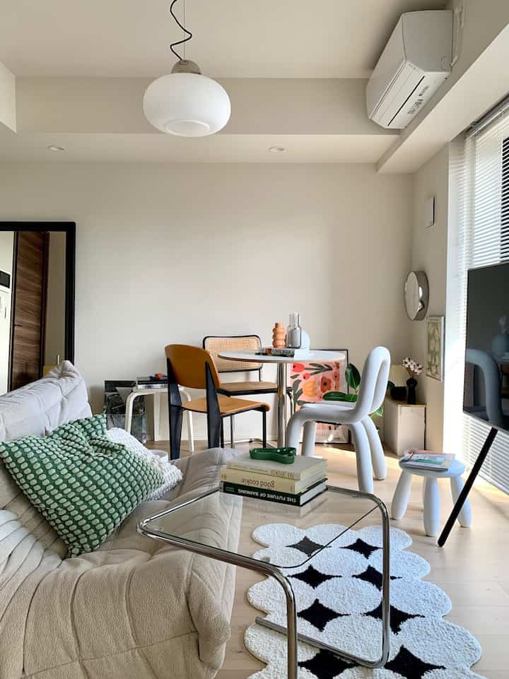 白とナチュラルカラーのリビング・ダイニング、モダンなソファと透明なガラスのコーヒーテーブルが配置された雰囲気のある空間