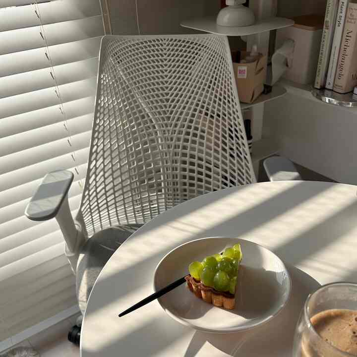 Bright white-toned home cafe with sunlight casting shadows on a round table featuring grape tart and a drink in a clean, modern setting